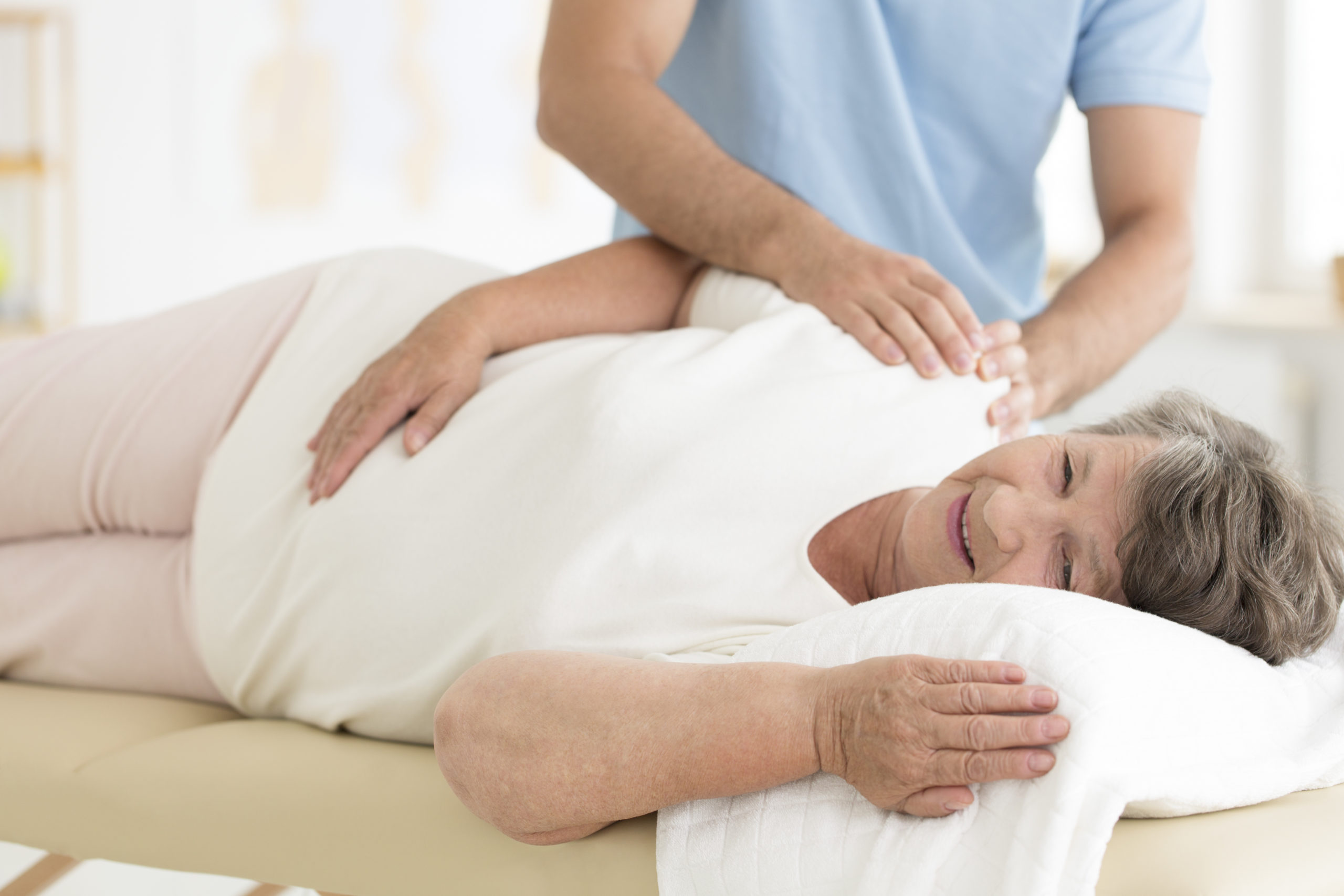 Professional masseur massaging shoulders of senior woman after an injury